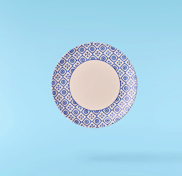 Levitating empty ceramic plate isolated on a pastel blue background. Minimalist zero gravity studio tableware photography concept.