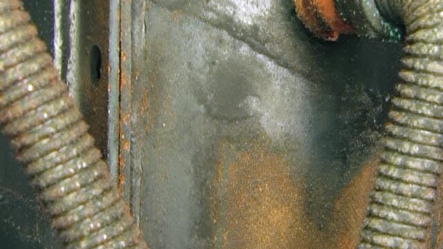 Close observation of heavily corroded industrial air filter system in workshop. Rusty metal plates, bolts, and flexible conduits show years of wear and tear, highlighting grime of heavy machinery.