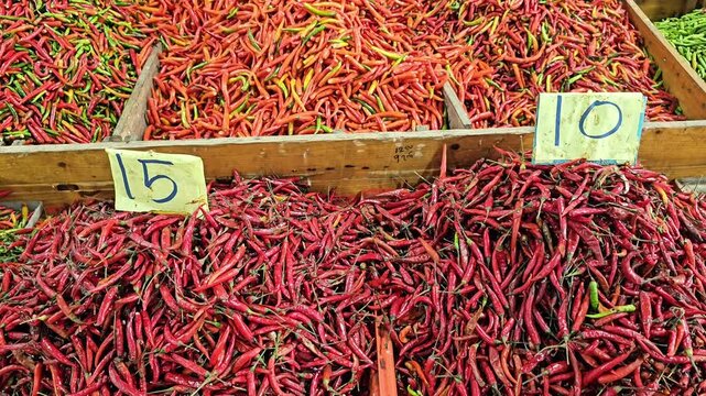 Large assortment of red and green chili peppers in wooden market boxes with handwritten price signs, fresh spicy vegetables displayed in street market stall, top view of produce arrangement