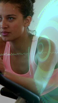Vertical video: Woman starting fitness on exercise bike, pedaling harder while HUD tracking metrics