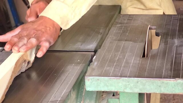 Carpenter using a professional jointer machine to smooth the edge of a wood plank in a bright carpentry studio High Quality Footage