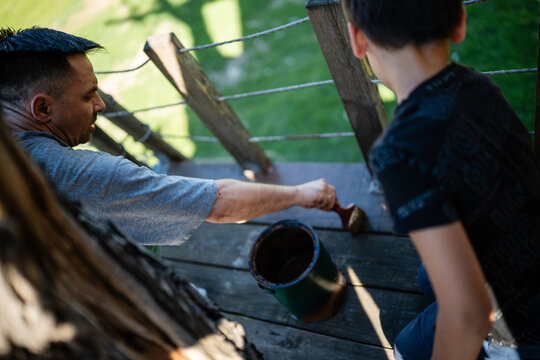 Father and son painting wooden deck railing