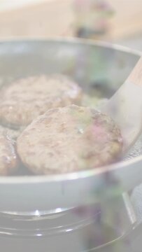 Vertical video: Cooking clip: spatula sliding under patty, flipping them for browning, oil sizzling
