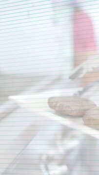 Vertical video: Hand with pink sleeve reaching with tongs, placing patties onto spatula for cooking
