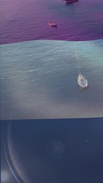 Vertical video: Shadow sweeping bay, flare causing boats drifting, white sailboat staying centered