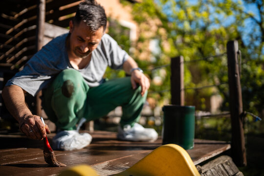Man staining wooden deck outdoors performing diy maintenance