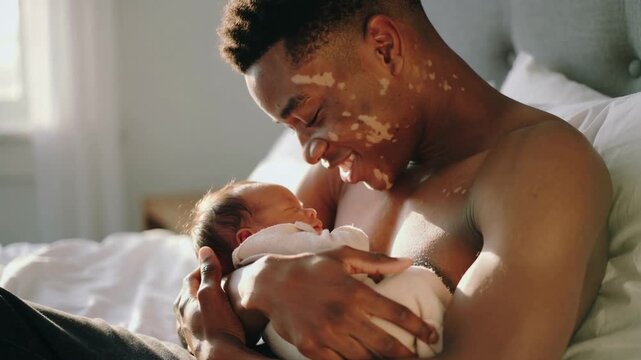 Black father with vitiligo holding his newborn baby in bed, medium shot, shallow depth of field