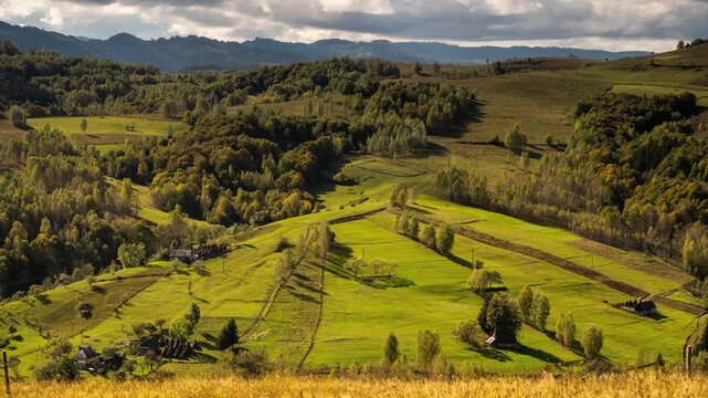 View of rolling green hills and autumn forests with traditional houses in Salciua de Jos, Alba County, Romania.