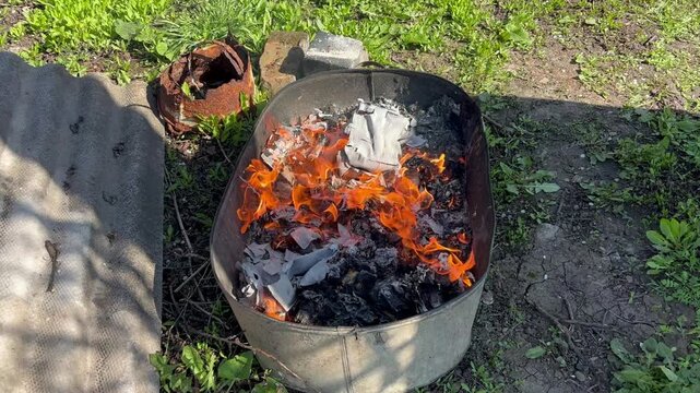 Burning trash and paper in outdoor fire pit, close-up flames and smoke
