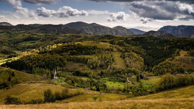 View of rolling green hills and a small white church nestled in the valley of Salciua de Jos, Alba County, Romania.