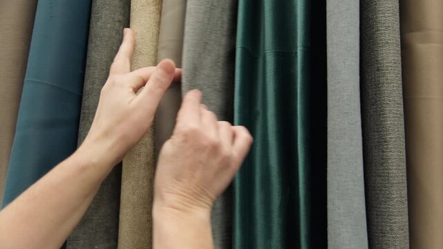 Woman hand flipping through fabric samples on display in showroom close-up, buyer chooses textile material