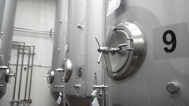 Stainless steel fermentation tanks in brewery with visible numbered valves and piping, showcasing industrial brewing equipment in action