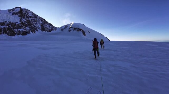POV mountaineering in rope team with mountaineers ascending towards mountain summit Naso del Lyskamm and glacier panorama in the morning in Pennine Alps, Italy