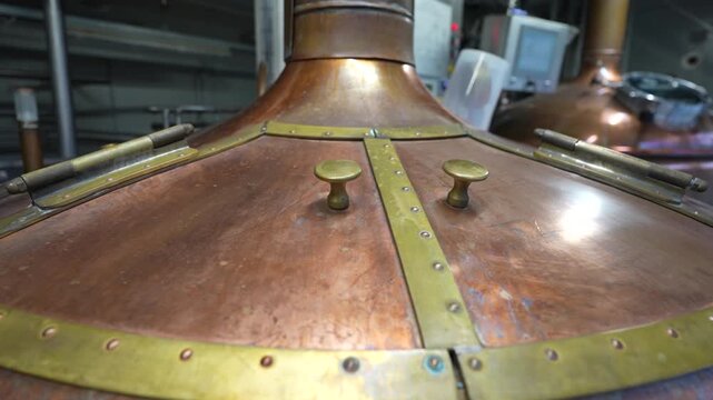 Copper brewing kettle with brass fittings in a brewery, showcasing detailed craftsmanship and industrial equipment in a well-lit environment