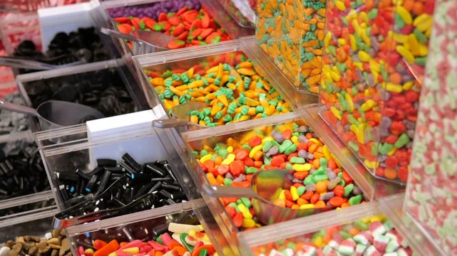 Multicolored assortment of delicious sweets, gummies, and licorice displayed in bulk bins with scoops at a candy store, showing a wide variety of flavors, shapes, and textures