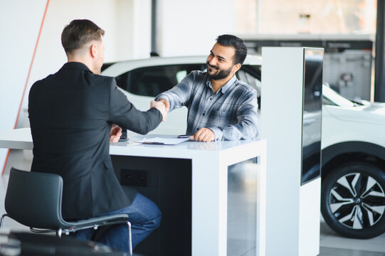 Client and salesman shaking hands sealing car deal at dealership