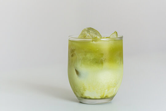 Matcha beverage with ice cubes in a clear glass, showcasing a layered green and cream appearance against a plain white background