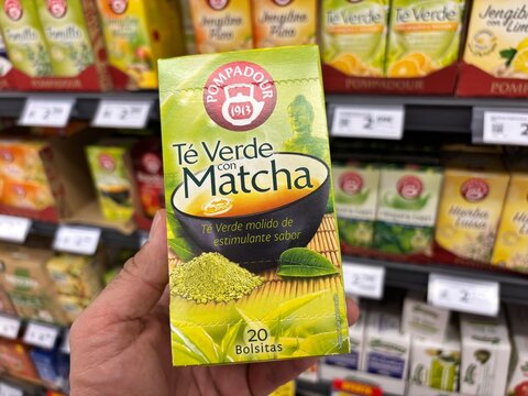 Alicante, Spain - April 25, 2026: Hand holding Pompadour green tea with matcha box in a grocery store aisle filled with various tea products in the background