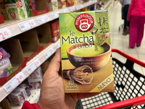 Alicante, Spain - April 25, 2026: Hand holding Pompadour matcha tea with lemon packaging in a grocery store aisle, shelves filled with various products in the background