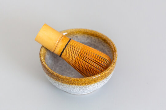 Matcha whisk made of bamboo resting inside a ceramic bowl with a speckled gray and gold design on a light gray surface
