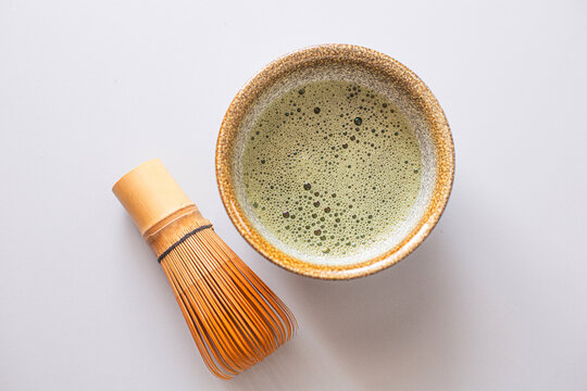 Matcha green tea in a traditional bowl with a bamboo whisk placed beside it on a light surface, showcasing the vibrant color and texture of the beverage