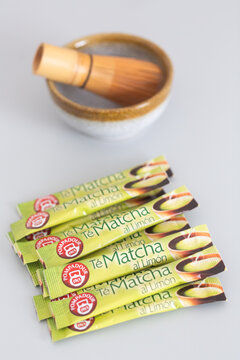 Alicante, Spain - April 25, 2026: Matcha tea powder packets with lemon flavor arranged beside a traditional bamboo whisk and ceramic bowl on a gray surface