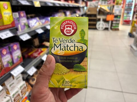 Alicante, Spain - April 25, 2026: Hand holding Ponapadur green tea with matcha box in a grocery store aisle, various products visible on shelves in the background