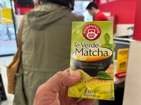 Alicante, Spain - April 25, 2026: Hand holding Pompadour green tea with matcha box in a store, customer and cashier visible in the background