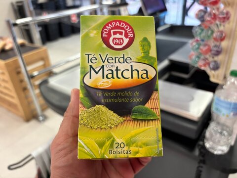 Alicante, Spain - April 25, 2026: Box of Pompadour green tea with matcha held in hand, featuring vibrant packaging and visible product details in a retail environment