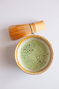 Matcha green tea in a textured bowl with a bamboo whisk placed beside it on a light surface, showcasing traditional Japanese tea preparation elements