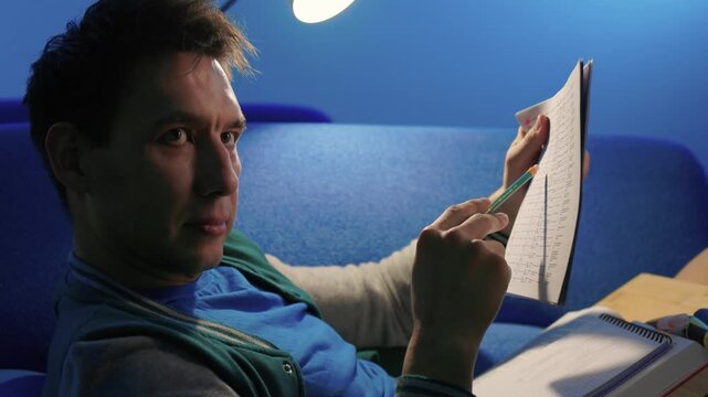 Individual concentrates while reviewing documents quietly. Lone individual carefully examines handwritten notes under gentle illumination during late night hours at home