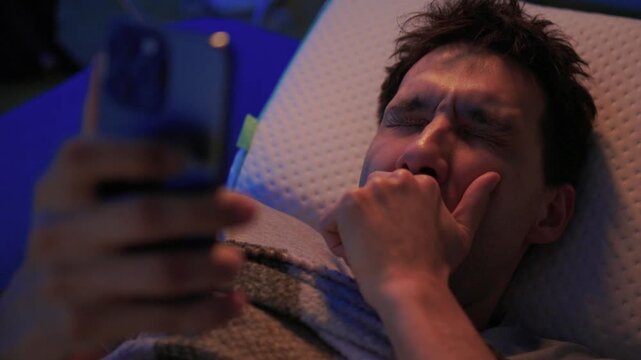 White man scrolling phone in bed, blue screen light on face, fingers tapping, checking messages and social apps, restless awake posture, blanket, late-night connectivity