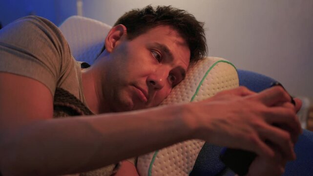 White man scrolling phone in bed, blue screen light on face, fingers tapping, checking messages and social apps, restless awake posture, blanket, late-night connectivity