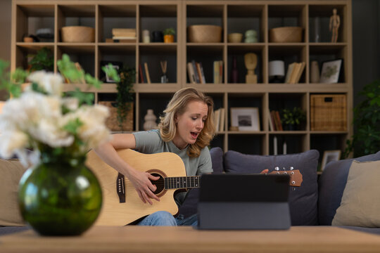 Woman practicing acoustic guitar and singing online lesson