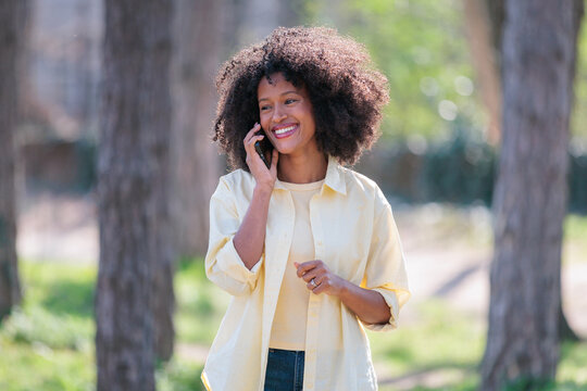 African woman speaks on phone in a park during daylight surrounded by trees and greenery