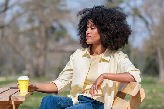 African woman enjoys coffee at a park while sitting on a bench in the afternoon