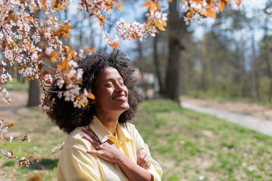 Young African woman enjoying flowers blooming in the park