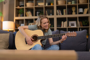 Obraz premium Woman playing acoustic guitar on sofa at home