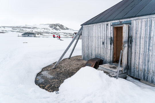 Svalbard, Svalbard and Jan Mayen - 21 June 2025: View of Kinnvika Station research base with wooden huts and people in red jackets standing on the snowy Arctic tundra.