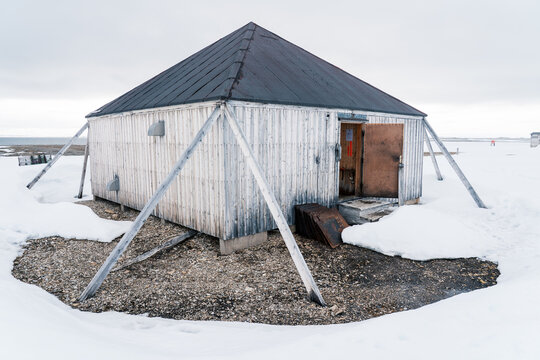 Svalbard, Svalbard and Jan Mayen - 21 June 2025: View of Kinnvika Station, a white wooden research building with a dark pyramid roof and diagonal supports surrounded by snow and gravel.