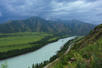 Obraz premium Scenic river valley with lush green hills and dramatic sky in serene mountain landscape