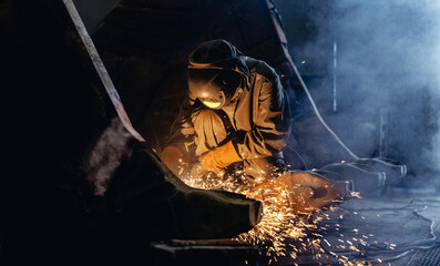 Welder cutting metal producing sparks in dim industrial workshop, recovery work for excavator bucket © Parilov