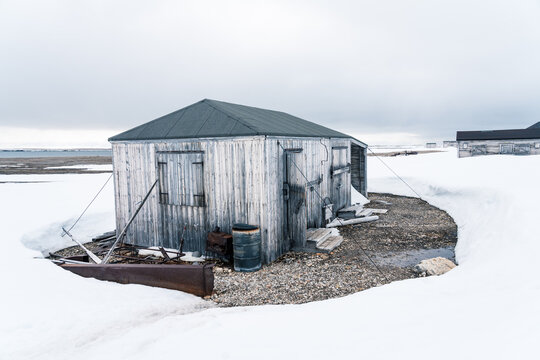 Svalbard, Svalbard and Jan Mayen - 21 June 2025: View of the historic Kinnvika Station wooden hut surrounded by melting snow and gravel under an overcast sky.