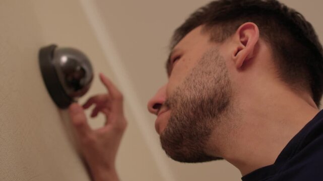 Technician installs indoor dome camera. Camera technician secures mounting and tests wiring. Security system installer calibrates lens and adjusts wiring carefully