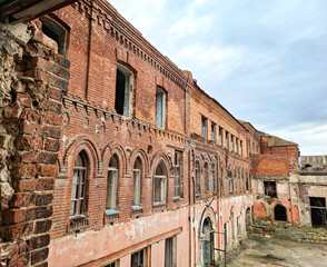 Fototapeta premium Decaying historic industrial building with weathered brick and arched windows under grey sky