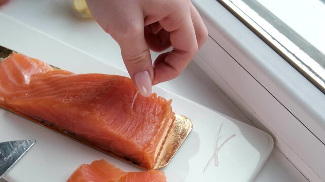 Woman hands carefully take bones out of sliced lightly salted red fish. Home kitchen preparation, salmon fillet ready for serving or cooking.