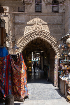 Cairo, Egypt - 20 April 2026: View of Khan el-Khalili bazaar featuring an ornate stone archway with a person standing in the shadows among traditional lanterns and textiles.