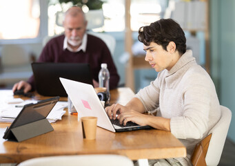 Fototapeta premium Men sitting at desk is working on laptop computer. Day in office of business structure, manager working at computer. Regional representative office of international company