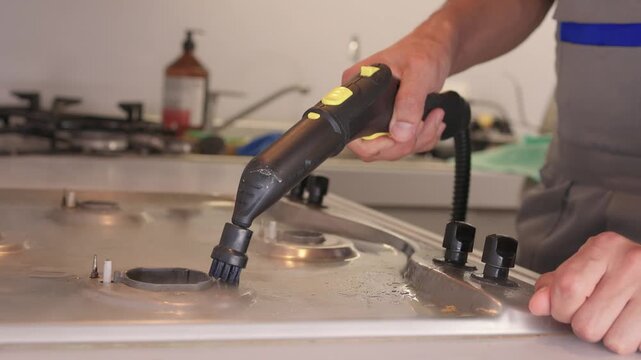 Handheld steam cleaner on stove top, powerful steam loosening burnt grease from stainless surface, closeup of nozzle and hand motion, countertop background, satisfying deep clean