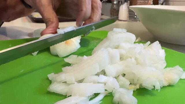 Close-up of hands chopping onions on a cutting board while preparing butter and onions for homemade pierogies in a kitchen setting. 15125  
